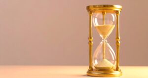 Golden hourglass timer with sand flowing from top to bottom on a warm beige background.